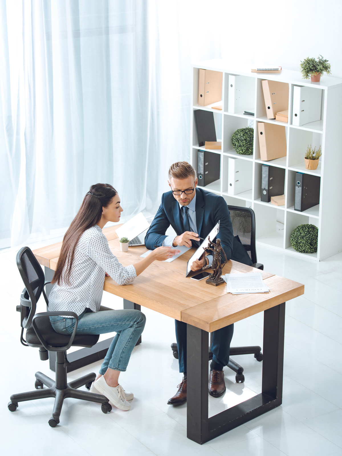 Professional meeting between a lawyer and client discussing documents in a modern office with legal files and decor in the background.