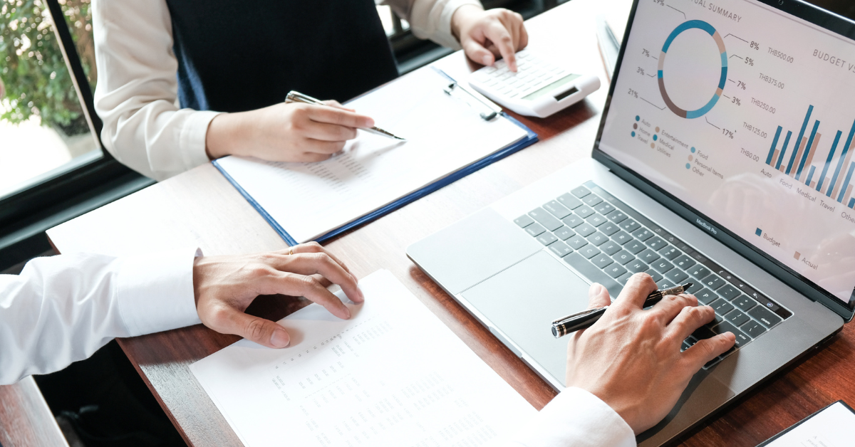 2 people look over notes on laptops and paper. Their heads are out of view