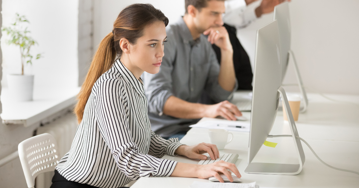 A woman writing on a computer in an office setting.
