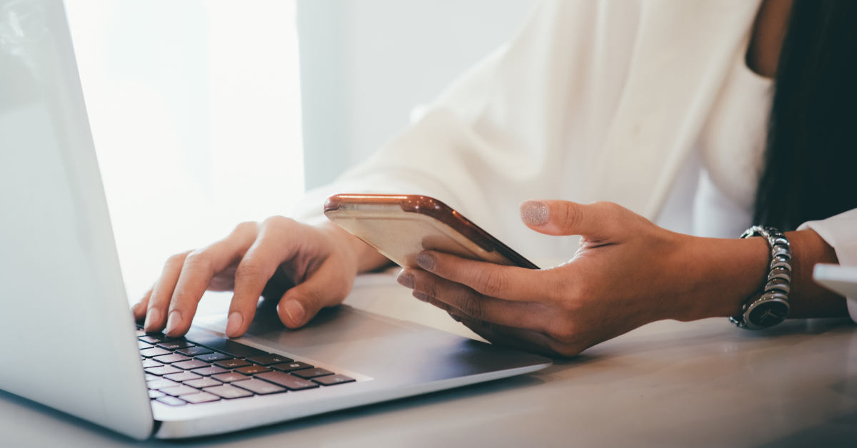 A woman using a laptop while also using her phone's touchscreen.