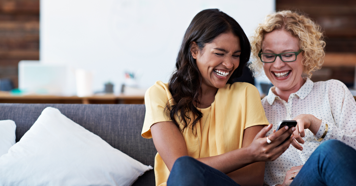 two women laughing at something they see on a phone