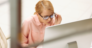 A woman working on a computer while adjusting her glasses.