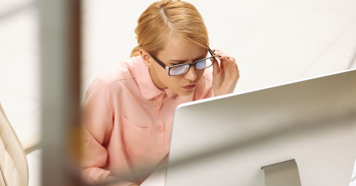 A woman working on a computer while adjusting her glasses.