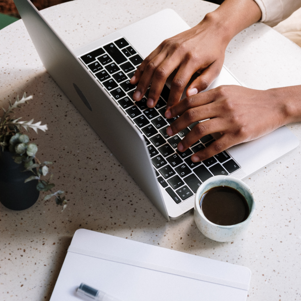 A person typing on a laptop with a cup of coffee next to them