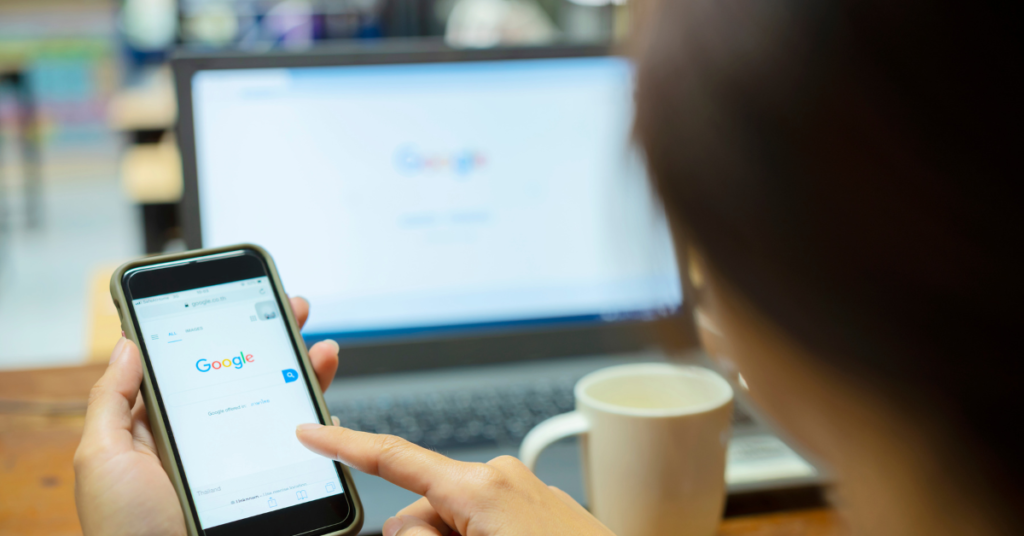 A phone displaying "google" while an out of focus computer screen in the back also displays "google"