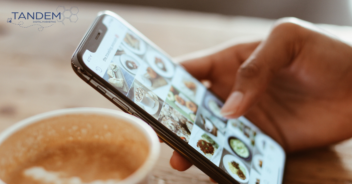 Person scrolling through Instagram on their phone with a coffee at a table.