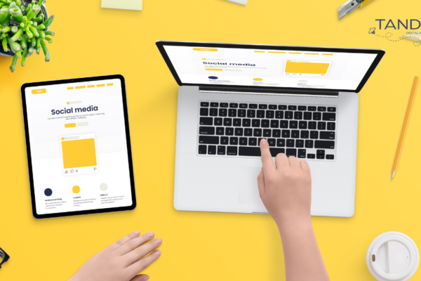 meta ads targeting A person is working on social media content on a laptop and tablet, surrounded by office supplies on a yellow desk.