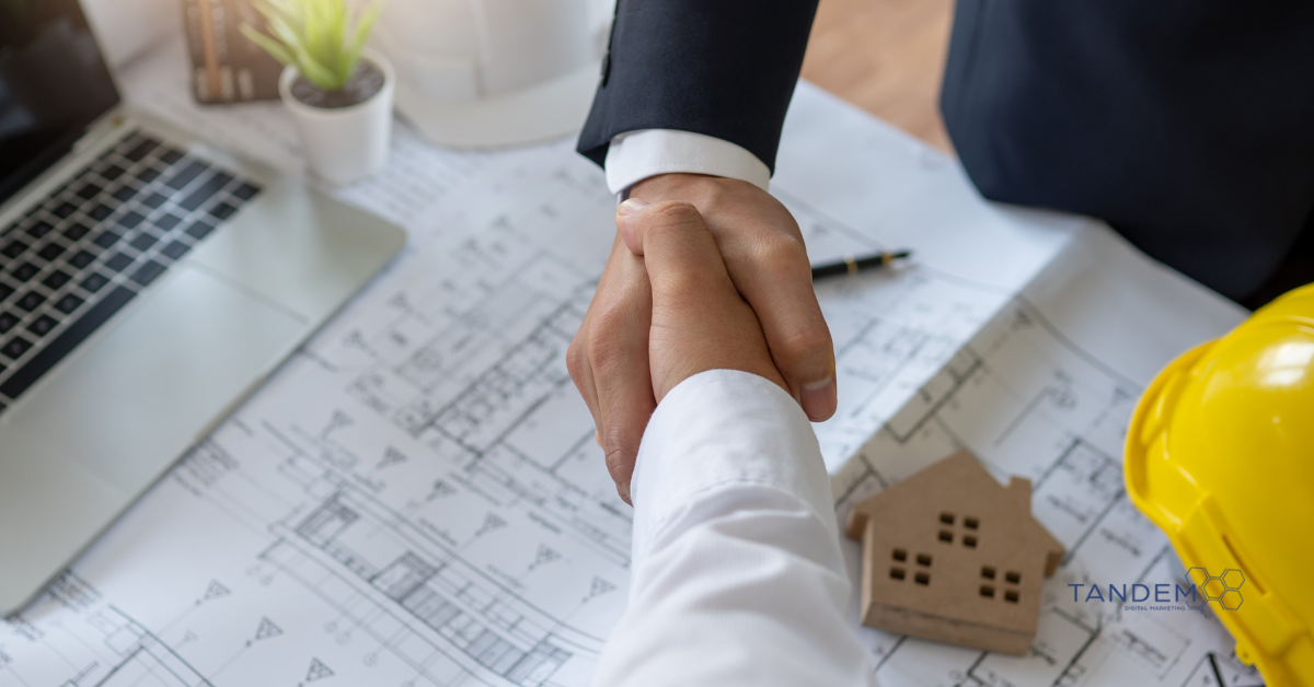 Two professionals shaking hands over real estate blueprints, with a miniature house model, hard hat, and laptop in view; Tandem Digital Marketing logo visible.