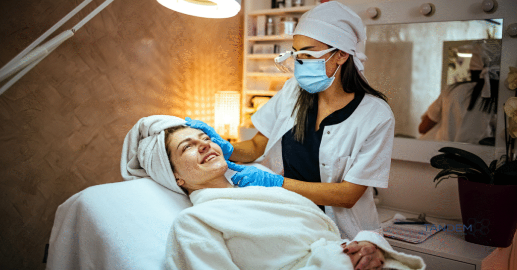 Dermatologist performing a facial treatment on a smiling patient in a spa-like clinic, with Tandem Digital Marketing branding visible in the corner.