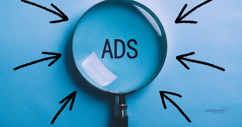 Magnifying glass highlighting the word "ADS" on a blue background with black arrows pointing inward, symbolizing ad targeting and visibility; Tandem Digital Marketing logo in the corner.