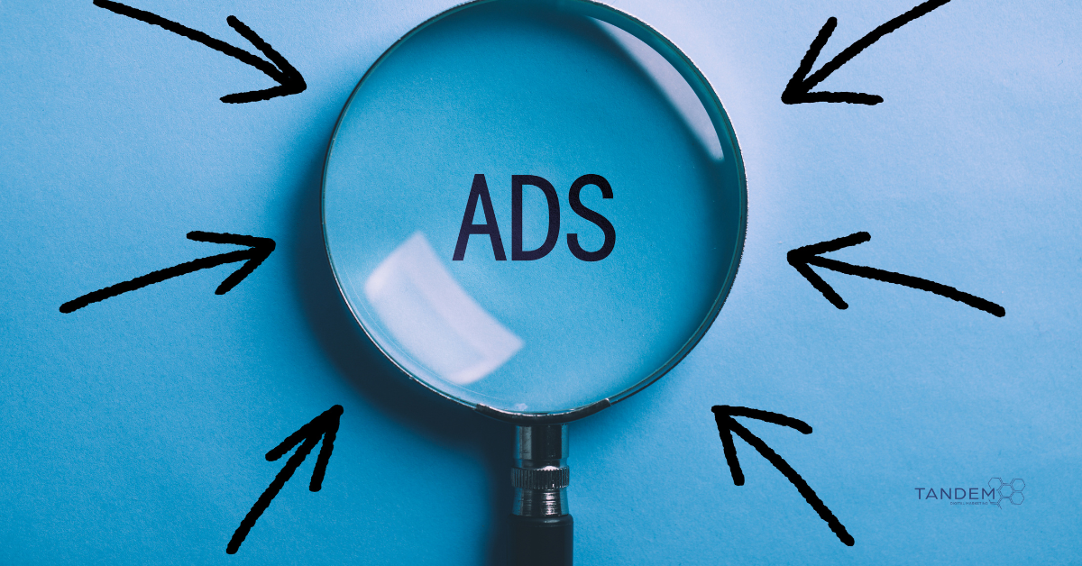 Magnifying glass highlighting the word "ADS" on a blue background with black arrows pointing inward, symbolizing ad targeting and visibility; Tandem Digital Marketing logo in the corner.