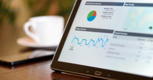Digital Marketing Metrics and Web Traffic Analytics Overview A close up of a tablet screen displaying digital marketing traffic source overview pie charts, visitor trends, and data metrics on a wooden conference table with a coffee cup in the background.