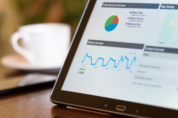 Digital Marketing Metrics and Web Traffic Analytics Overview A close up of a tablet screen displaying digital marketing traffic source overview pie charts, visitor trends, and data metrics on a wooden conference table with a coffee cup in the background.