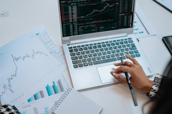 August 2026 Digital Marketing Updates and Financial Data Analysis A high-angle view of a professional digital marketing strategist analyzing printed financial charts and laptop data metrics for Tandem Interactive’s August 2026 digital marketing updates.