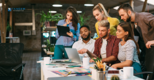 A collaborative team of digital marketing strategists gathered around a laptop reviewing campaign performance metrics, featuring the new Tandem Interactive logo for our September digital marketing updates.